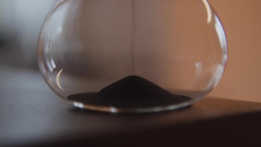 An hourglass rests on a wooden surface its sand steadily cascading from the upper chamber to the lower one