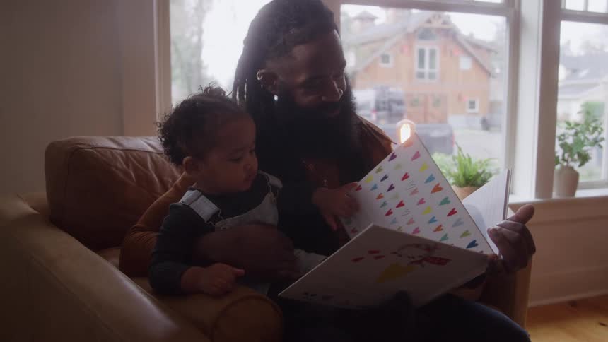 Father reading a book to his daughter in a sunlit room