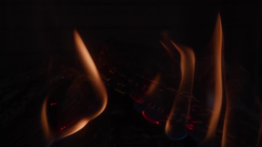 Multiple thin columns of orange and yellow flames rise vertically the flames flicker and undulate against a deep black background faint red embers glow at the base of the fire