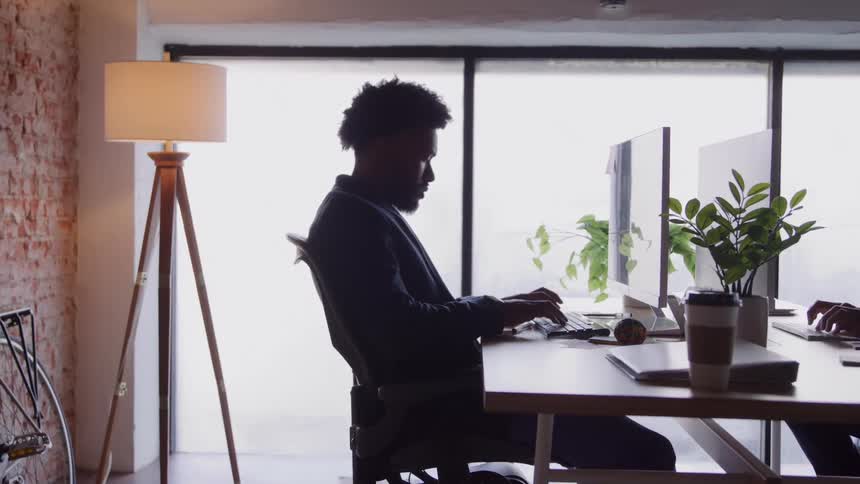Man works at a computer in an office lit by natural light