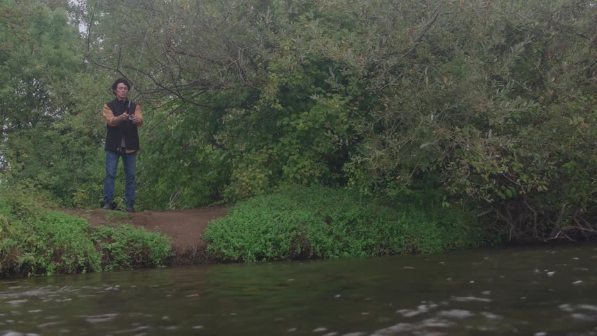 A young man fishing beside a flowing river outdoors during daytime