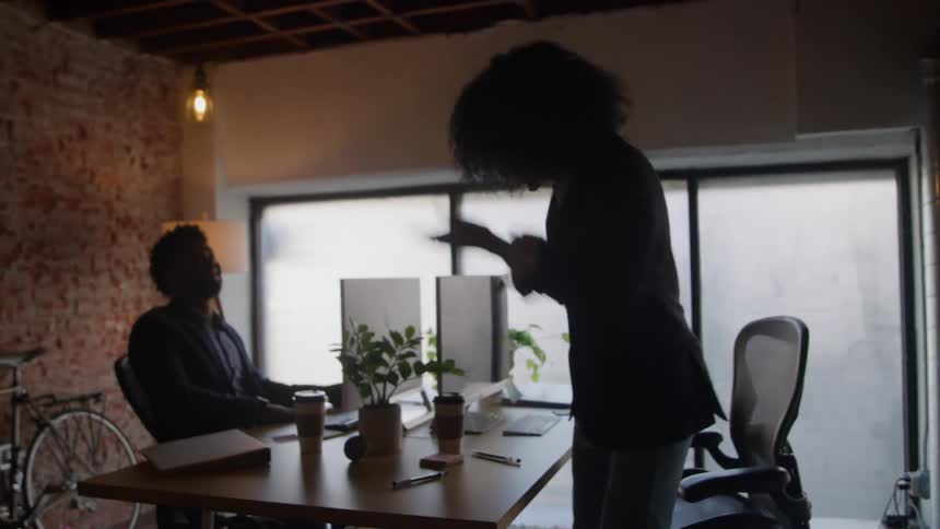 The woman enters the office and sits down at her desk while talking