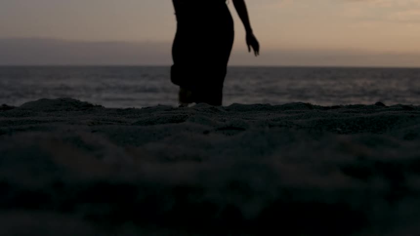 Silhouette of a person running on the sand during sunset by the sea
