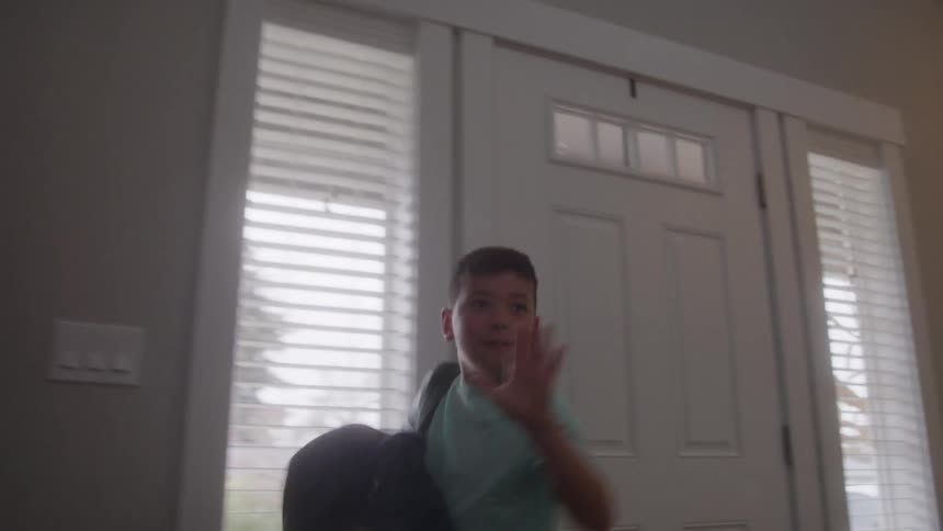 The boy waves as he leaves the home for school