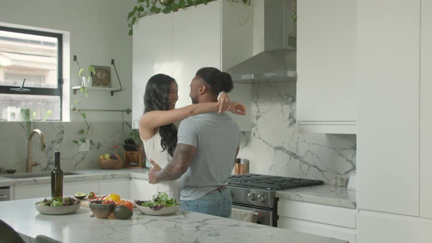 A young couple dancing together in a kitchen during daytime