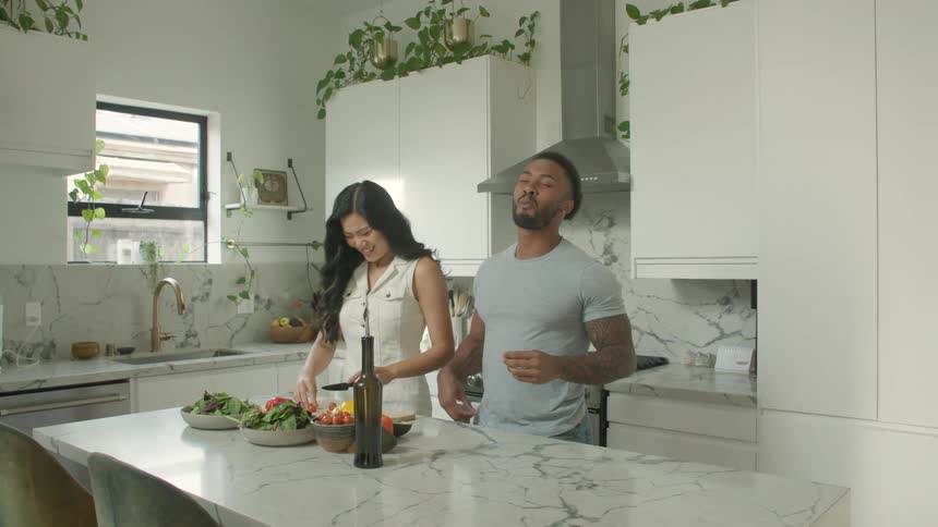 The woman feeds a man a piece of vegetable she cut