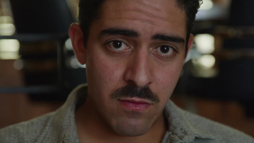 Young hispanic man sitting down with a nervous face expression indoors during day time