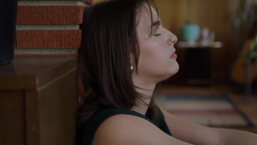 Woman leans against the wall with eyes closed in a moment of rest