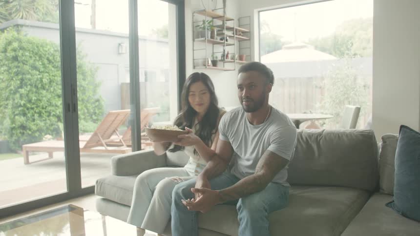 Couple relaxes on the couch watching a movie and eating popcorn