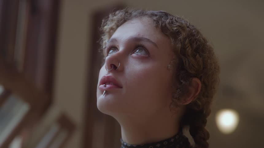 Close up portrait of a young woman looking upwards while standing in a room during daytime