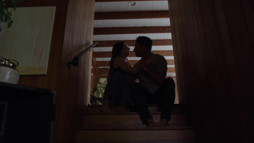 Young man and young woman sitting down on a staircase hugging and caressing each other indoors during day time