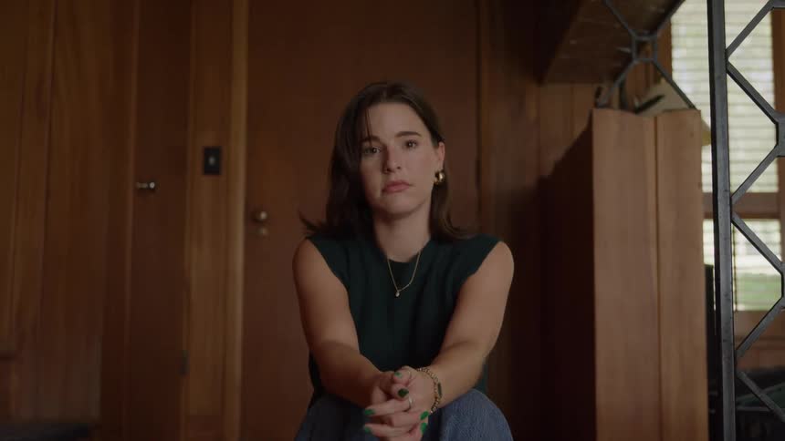 Young teenager woman sitting down indoors with a contemplative face expression during day time