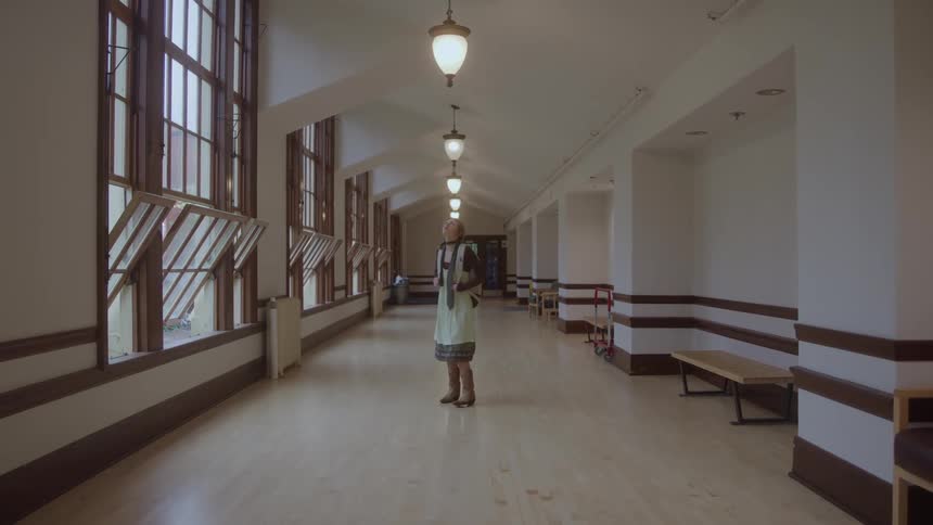 Young female person wearing glasses and carrying a backpack walking on a corridor and looking in all directions indoors during day time