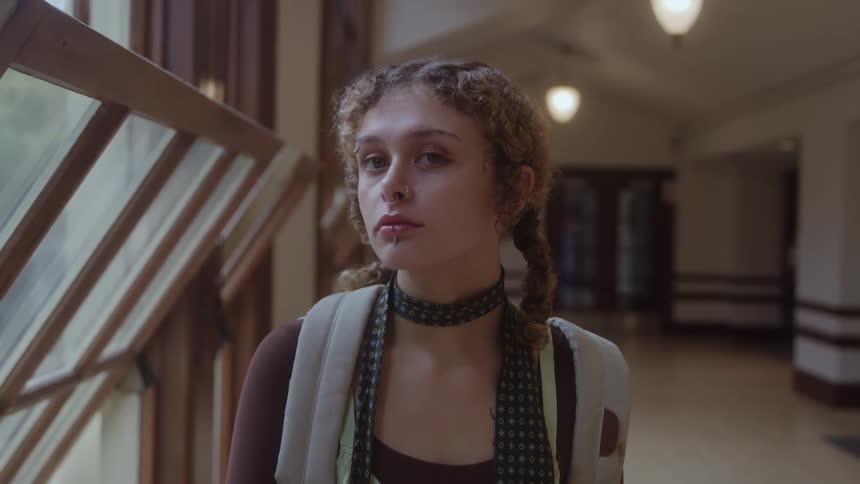 Student with a serious expression in a hallway lit by windows