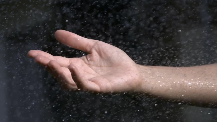 Close up of a persons hand under sprinkling water outdoors during daytime