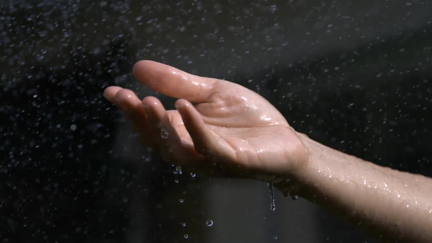 Outstretched hand catches raindrops under natural light