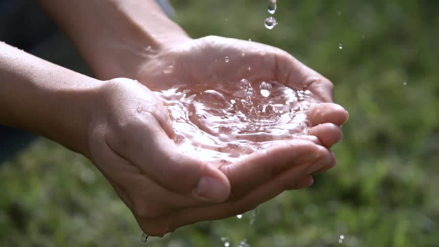 Cupped male hands collecting water that is dripping on them outdoors during day time