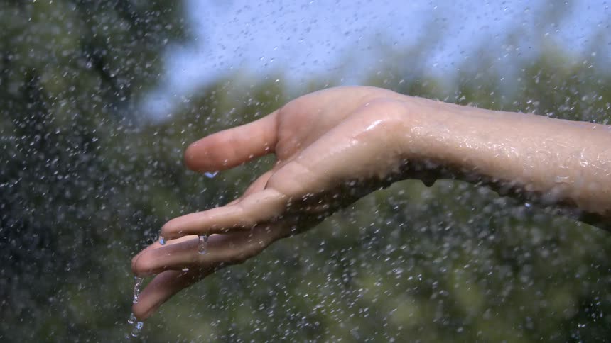 Outstretched hand feels the raindrops falling under the blue sky