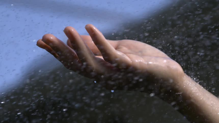 Hand raised catching raindrops under a blue sky