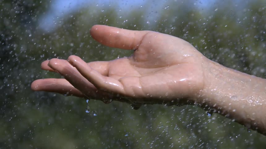 Drops of water falling over the hand of a white person outdoors during day time