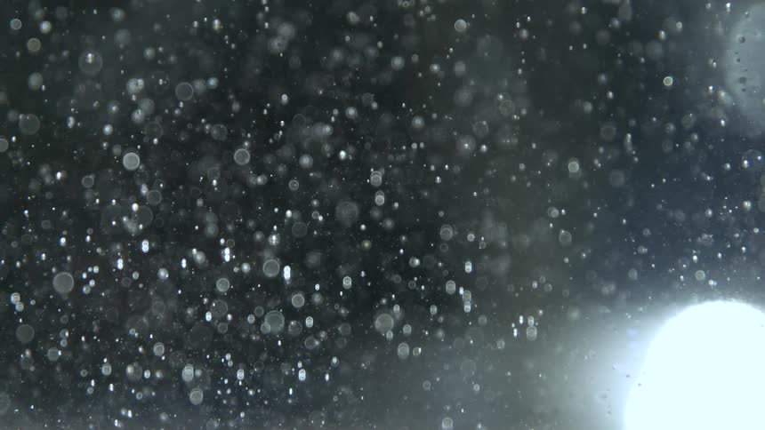 Snow particles in the air in front of a bright flashlight outdoors at night