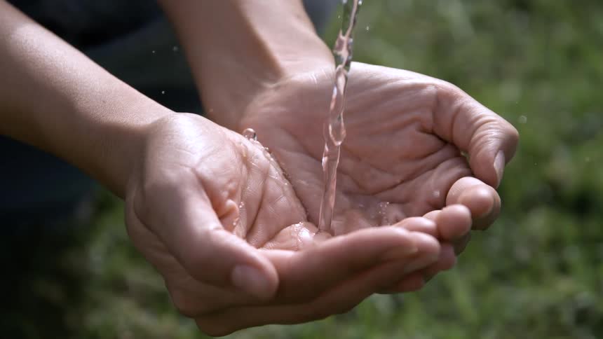 Close up of a person collecting flowing water in their palms outdoors during daytime