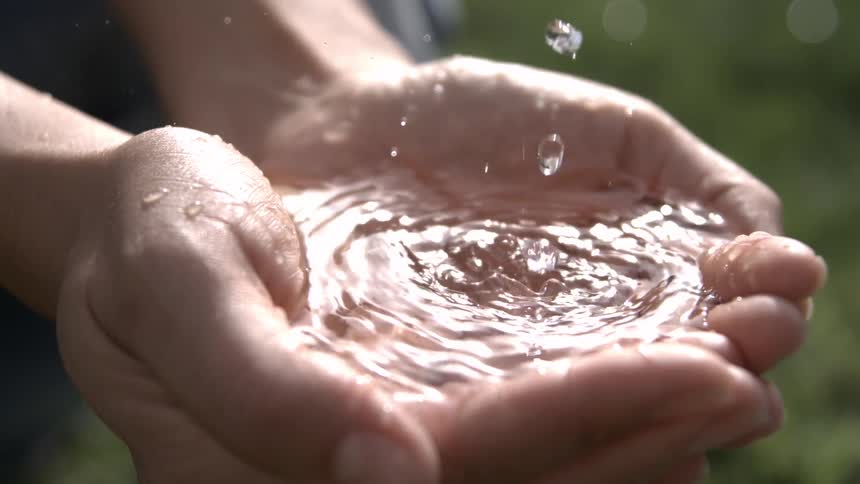 The video is an extreme closeup of a persons hands gently sifting fine sand through their open fingers the scene is at the waters edge on a beach at what appears to be sunset with the warm light illuminating the flow of sand
