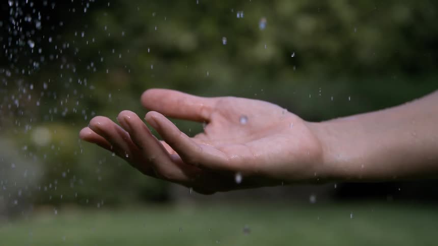 The video is an extreme closeup of a persons hands as they gently sift fine sand through their open fingers the scene is at the waters edge at what appears to be sunset with the warm light catching the flow of sand