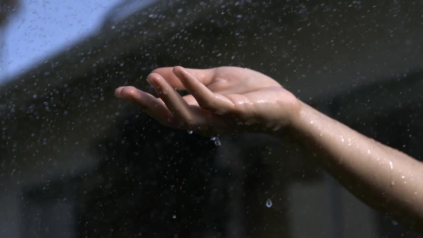 Hand outstretched under the rain on a clear day