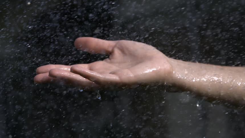 Outstretched hand catching raindrops under natural light
