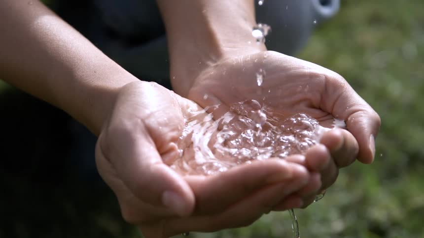 Cupped hands of a man with a pool of water and more water dripping on it outdoors during day time