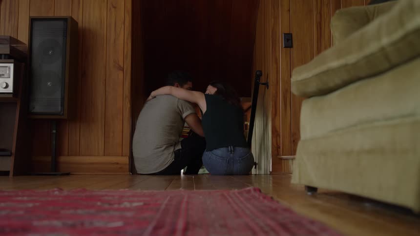 Woman sits next to man in wooden hallway offering support