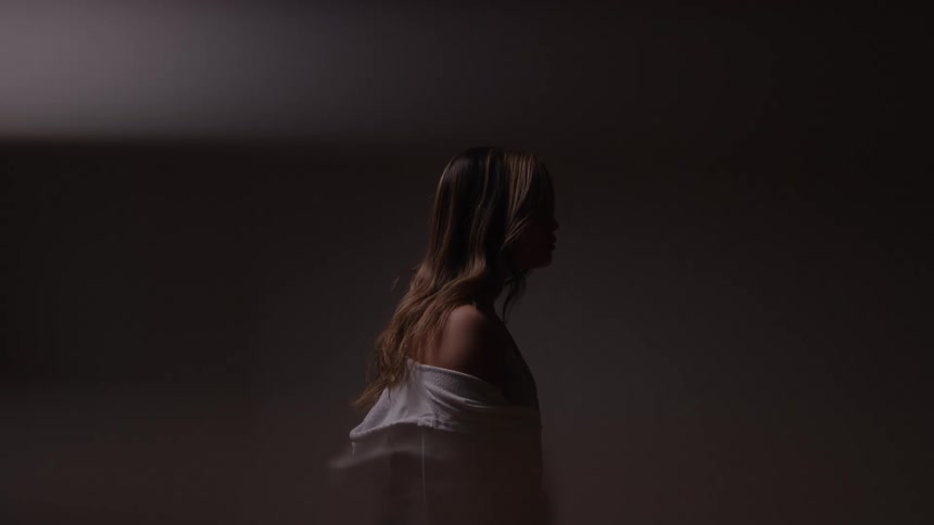 Woman walks in dim light with her gaze directed downward