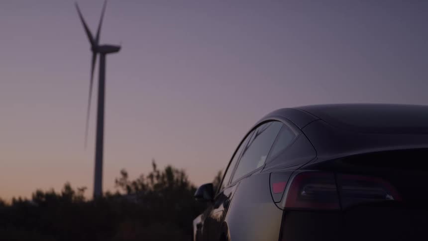 Tail light of a parked car turns on as a wind turbine spins in the distance