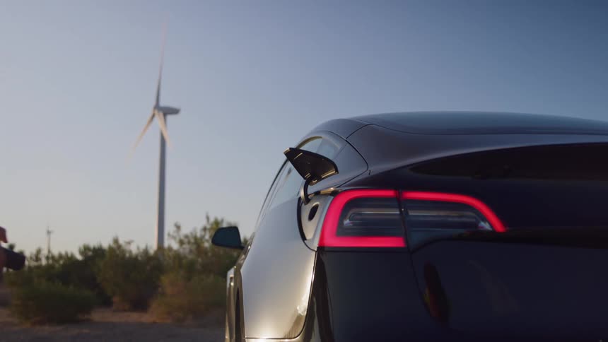 Woman disconnects charging cable from electric car under sunset light