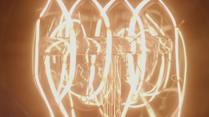 Incandescent filament glows brightly inside a light bulb in closeup