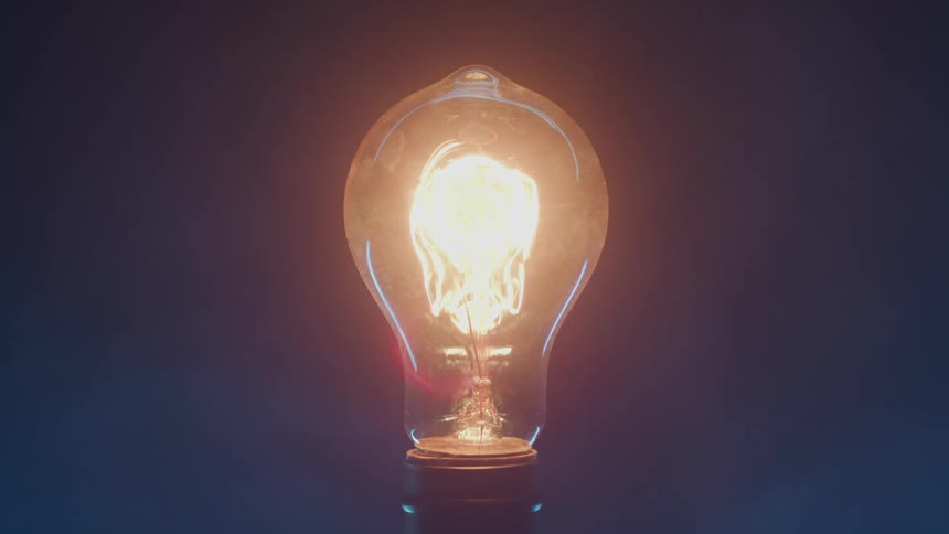 Lit light bulb with glowing filament against a dark background
