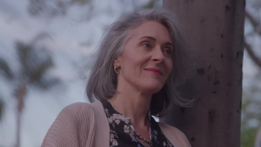 The woman smiles while leaning on the tree