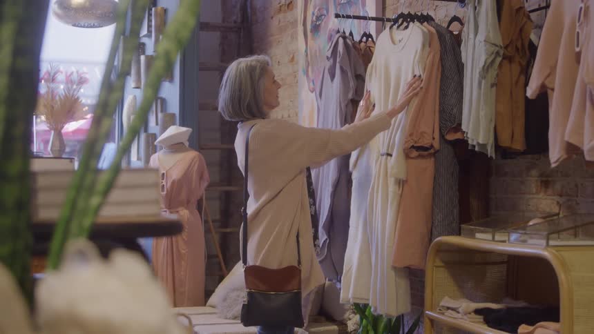 Grayhaired woman browsing clothes on a rack inside a boutique store