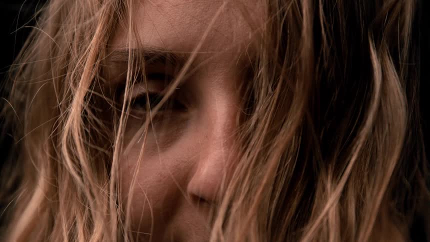 Loose hair partially covers the face illuminated by soft light