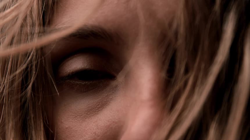 Long brown hair moves in the breeze across a womans face as she blinks her eyes