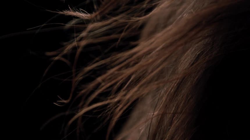 Strands of brown hair move gently against the dark background