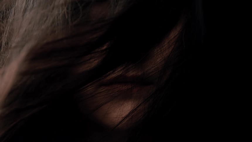 Strands of hair partially cover the face under soft lighting