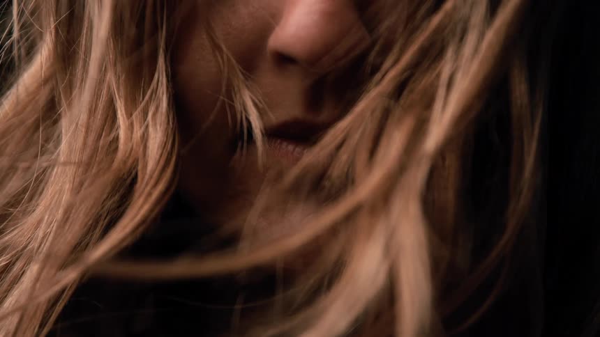 Strands of hair move across the partially lit face