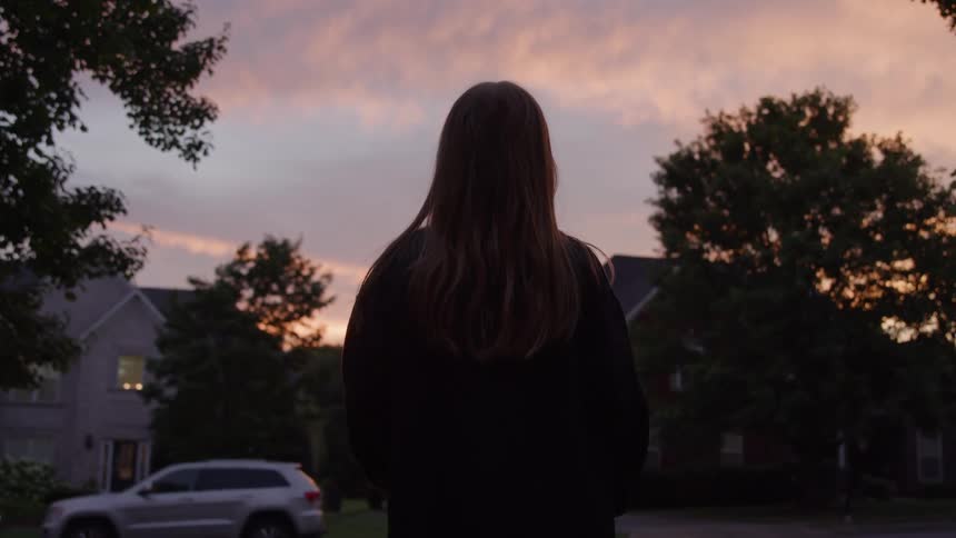 Woman watches the sky painted by the sunset in a residential neighborhood