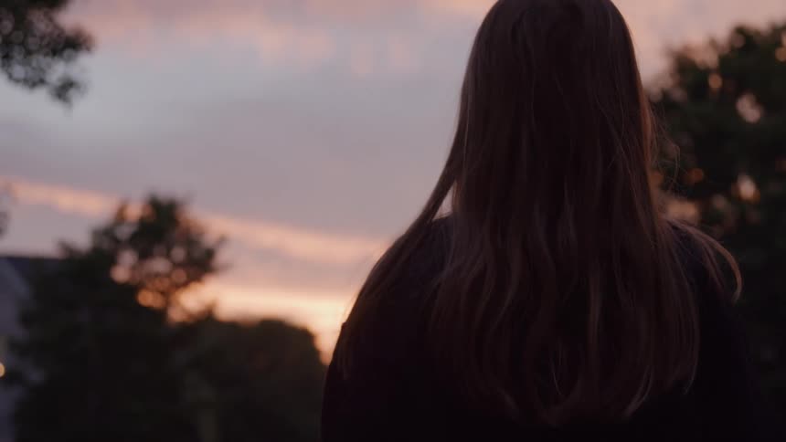 Close up of a young woman standing outdoors at sunset