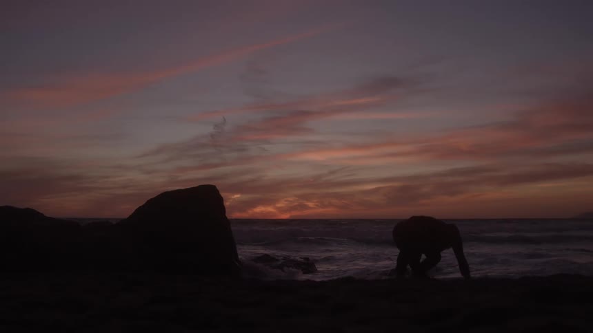 Man stands on a rock along the coast and jumps running across the beach