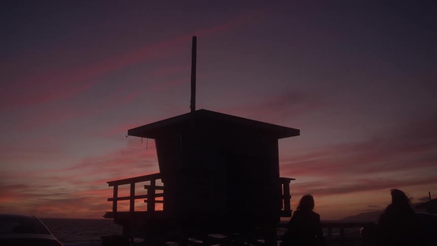 Two young women walk near a lifeguard tower on the beach