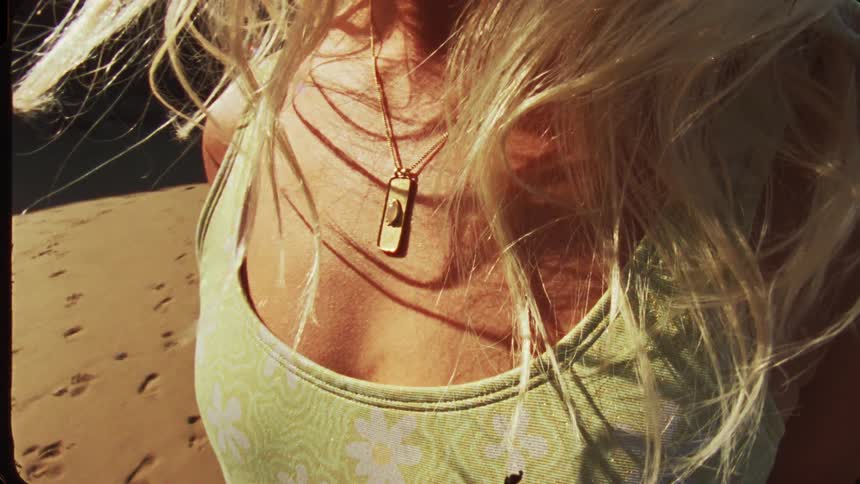 Sunlight illuminates a golden necklace over a green floral dress on the beach