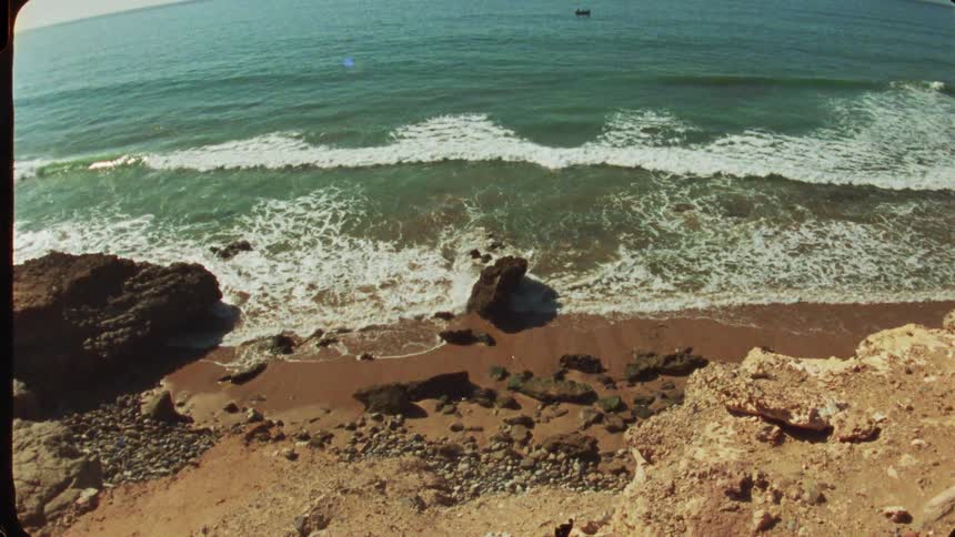 This short video shows an aerial view of a secluded beach and the oceanthe camera is positioned high above looking down at a small rocky cove where the waves crash onto the shorethe water is a bright turquoise blue contrasting with the dark brown